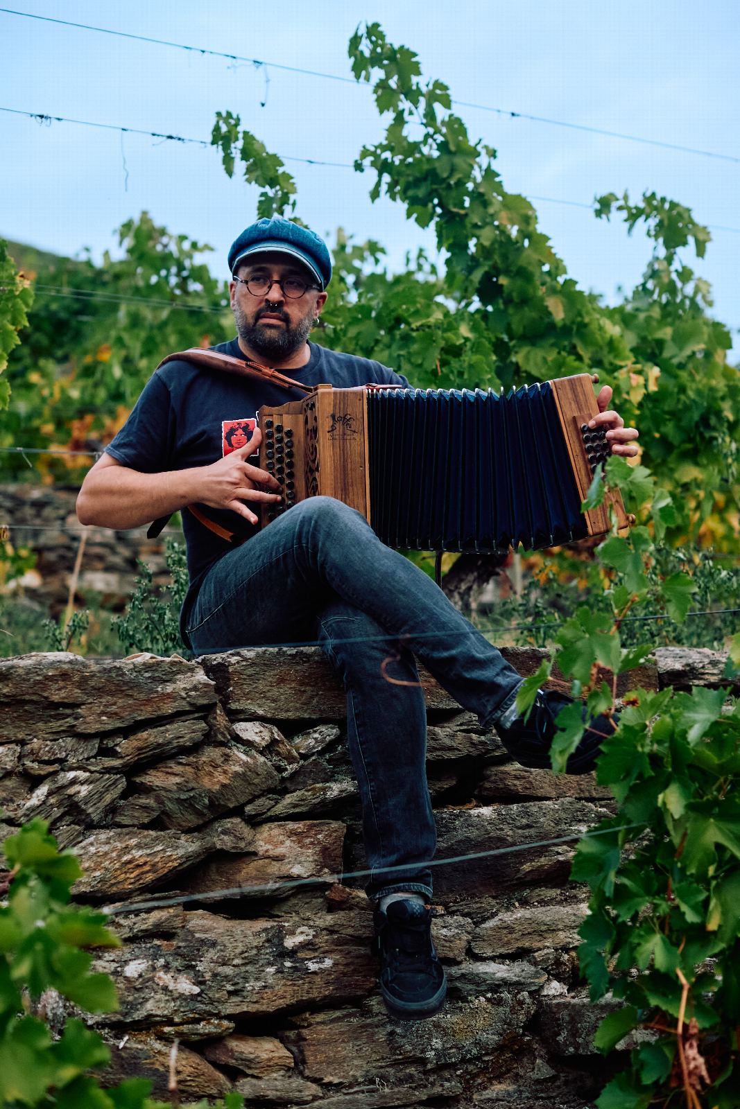 Un músico toca o acordeón sentado nun muro da viña