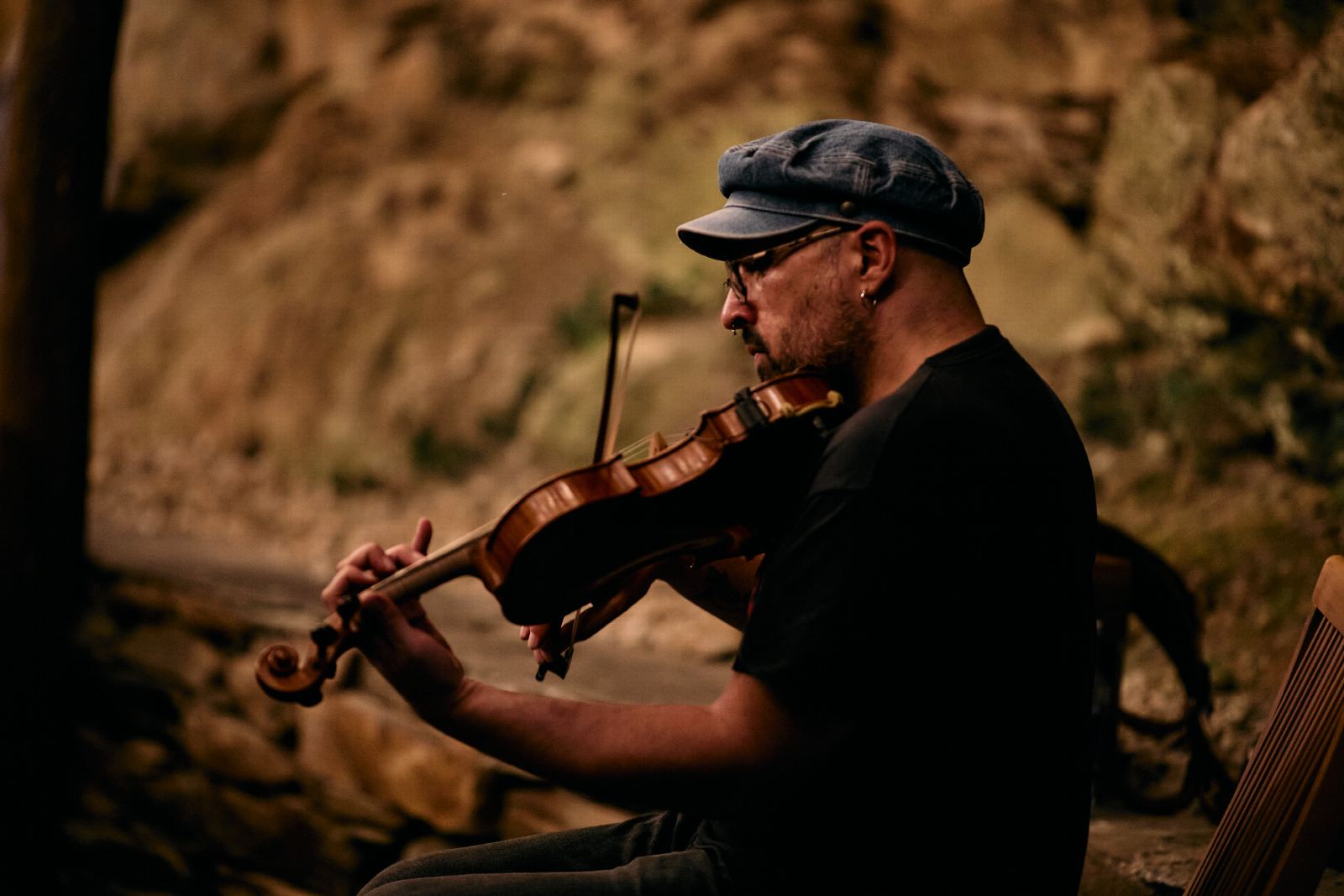 Un músico toca o violín xunto a un muro de pedra